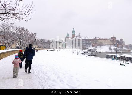 Polnische Familie - eine Familie mit Kindern, die im Winterschnee am Weichsel-Fluss spazieren geht, mit Wawelschloss im Hintergrund; Krakau Polen Europa Stockfoto