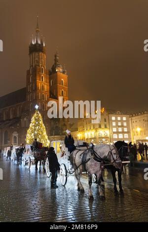 Reisen Sie nach Krakau; Hauptmarktplatz bei Nacht, mit beleuchteter St. Marys Kirche und Pferd und Kutsche zu Weihnachten für den Weihnachtsmarkt, Krakau Polen Stockfoto