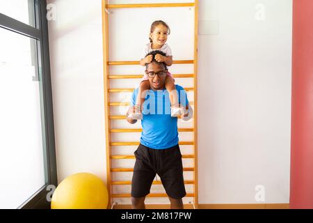 Vater spielt mit seiner Tochter und hält sie im Fitnessstudio auf den Schultern Stockfoto