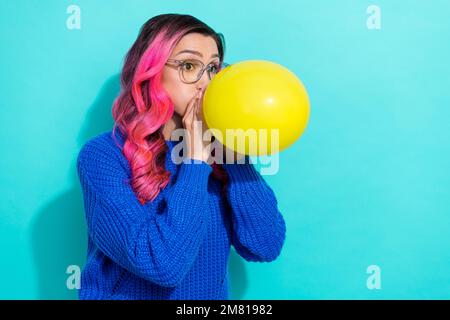 Foto eines jungen, lustigen Mädchens, das einen gelben Luftballon bläst Kleidung blau gestrickte Pullover Vorbereitung Feier Party isoliert auf aquamarinfarbenem Hintergrund Stockfoto