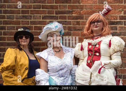 Porträt von drei Frauen, weibliche Steampunks, lächelnd, während sie neben einer Wand standen. In historischen Kostümen gekleidet, Steampunkkleidung. Stockfoto