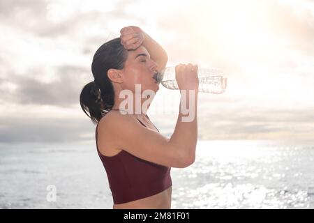 Sportliche Frau, die nach dem Training an einem heißen Tag Wasser trinkt. Weibliche Athlite nach dem Workout. Stockfoto