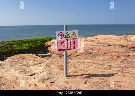 Hilbre Island, Großbritannien: Warnschild auf felsigem Felsvorsprung mit der Dee-Flussmündung darunter. Gefahr – Abstand zu überhängenden Felskanten halten, Abstand halten Stockfoto