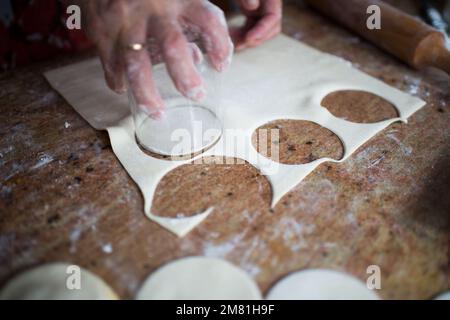 Menschliches Handschneiden von rundem Blätterteig mit einem Glas. Schließen Stockfoto