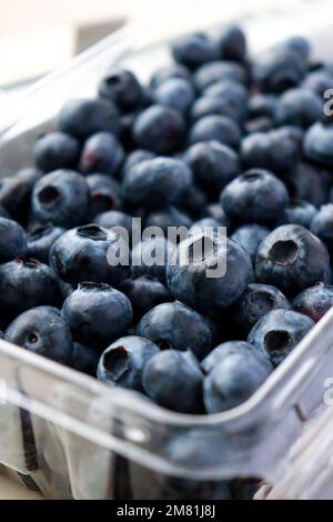 Nahaufnahme frischer Blaubeeren in einer Plastikbox, weißer Tisch Stockfoto