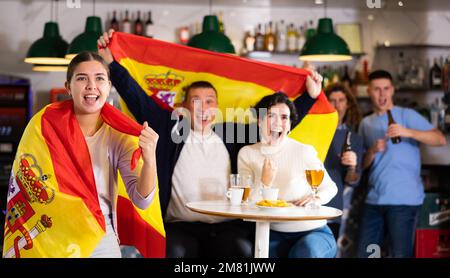 Begleitung von aufgeregten jungen Sportfans, die die Flagge Spaniens schwenken und die Nationalmannschaft mit Bier im Pub unterstützen Stockfoto