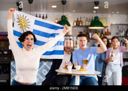 Fans mit der Flagge Uruguays feiern den Sieg ihrer Lieblingsmannschaft in der Bierstube Stockfoto