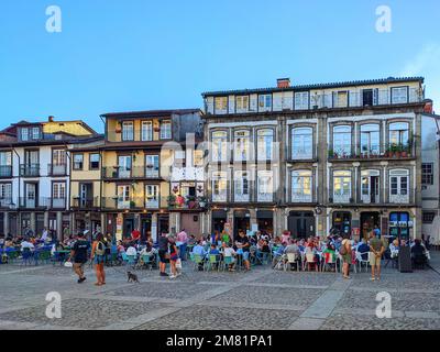 Menschen in Straßencafés am Hauptplatz von Guimaraes, traditionelle portugiesische Architektur, Portugal Stockfoto