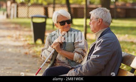 Blinde ältere Frau mit ihrem Mann, der auf einer Bank im Park sitzt. Hochwertiges Foto Stockfoto