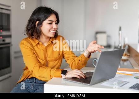 Lächelnde Junge Arabische Frau, Die Videoanrufe Mit Einem Laptop In Der Küche Macht Stockfoto