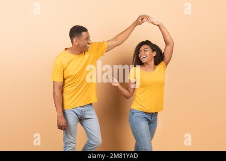 Fröhliches afroamerikanisches Paar, das auf gelbem Hintergrund tanzt, glückliche, romantische schwarze Ehepartner, die Spaß miteinander haben Stockfoto