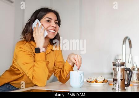 Wunderschöne Junge Arabische Frau, Die Auf Dem Handy Spricht Und Kaffee In Der Küche Trinkt Stockfoto