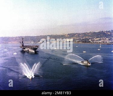 Eine Luftaufnahme von Steuerbord auf den Flugzeugträger USS RANGER (CV 61), der von einer WESTPAC-Kreuzfahrt nach San Diego zurückkehrt. Im Vordergrund spritzen Hafenschlepper Wasser in die Luft, um den RANGER wieder willkommen zu heißen. Basis: San Diego Staat: Kalifornien (CA) Land: Vereinigte Staaten von Amerika (USA) Stockfoto