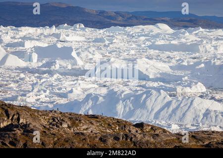 Die Leute beobachten große Eisberge, die über dem Meer schweben Stockfoto