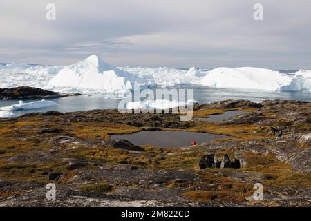 Ein Mann beobachtet große Eisberge, die über dem Meer schweben Stockfoto