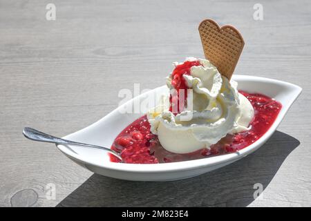 Vanilleeis mit Schlagsahne und rotem Gruetze, eine rote Fruchtgelee aus Deutschland und Dänemark, Sommerdessert in einer weißen Schüssel auf einem grauen Tisch, Polizist Stockfoto