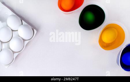 Werkzeuge zum Malen von ostereiern, Eierschachtel, Tassen mit bunten Farben, ostereier, Teller, Pinsel und Farben auf der Seitenansicht des Tisches. Stockfoto