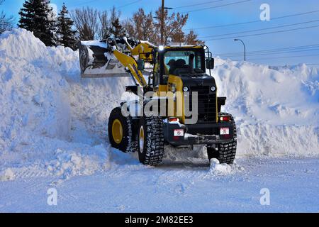 Der Frontlader kann große Mengen Schnee auf dem Parkplatz des Einkaufszentrums aufsammeln. Stockfoto