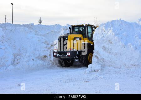 Der Frontlader kann große Mengen Schnee auf dem Parkplatz des Einkaufszentrums aufsammeln. Stockfoto