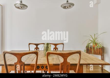 Ein Esstisch und Stühle in einem Raum mit weißen Wänden, Holzböden und Holzfußboden. An der Wand befindet sich eine Pflanze Stockfoto