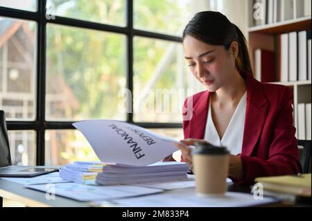 Professionelle und konzentrierte asiatische Geschäftsfrau, die an ihrem Schreibtisch einen Geschäftsbericht liest. Stockfoto