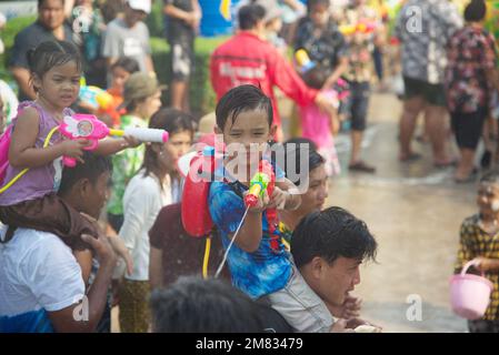 Ein unidentifizierter kleiner Junge sitzt auf dem Hals seines Vaters und spielt Wasserspray mit einer Plastikpistole. Nehmen Sie am Songkran Festival, dem traditionellen Neujahrsfest, Teil. Stockfoto