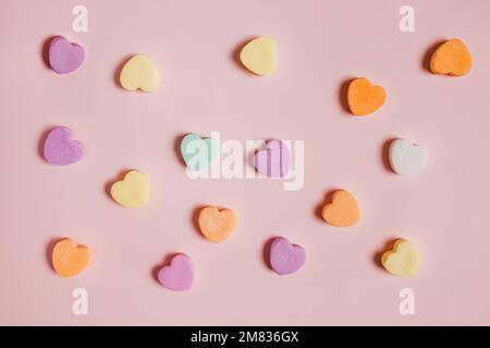 Farbenfrohe herzförmige Süßigkeiten auf pastellrosa Hintergrund, Valentinstag-Kulisse Stockfoto