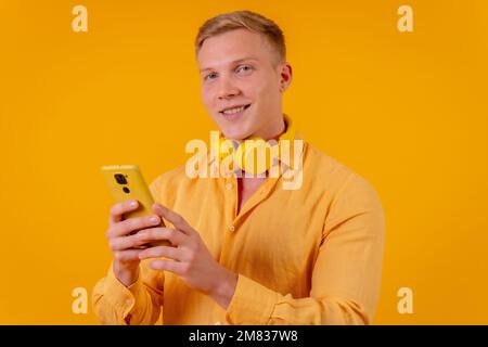 Ein blonder Kaukasier, der Musik mit einem Telefon auf gelbem Hintergrund auswählt Stockfoto