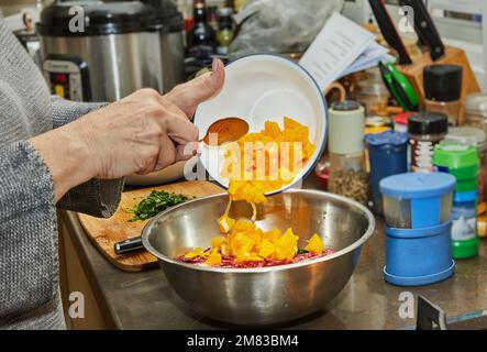 Der Koch verwandelt die Orangen in einen Salat mit Zucchini, Orangen und Salami. Französische Gourmetküche im Holzhintergrund. Stockfoto