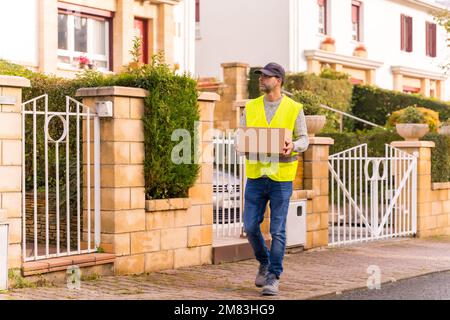 Ein Paketzustelldienst mit einer Schachtel aus einem Online-Shop vor einem Haus Stockfoto