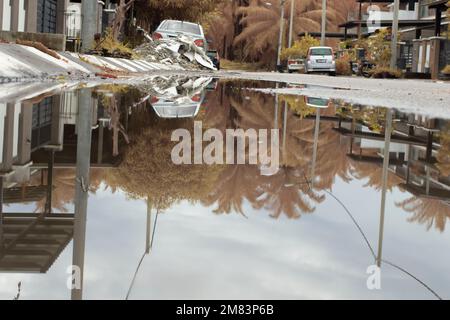 Stagnierende Wasserszene nach Regen in der vorstädtischen Asphaltstraße Stockfoto