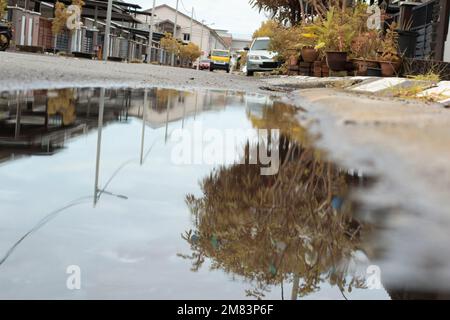 Stagnierende Wasserszene nach Regen in der vorstädtischen Asphaltstraße Stockfoto