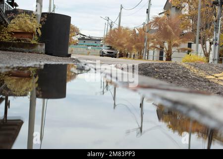 Stagnierende Wasserszene nach Regen in der vorstädtischen Asphaltstraße Stockfoto