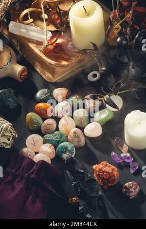 Hexenausrüstung auf schwarzem Hintergrund. Esoterischer okkulter Altar mit Runensteinen, Kristallen, Kerzen, altem Buch umhüllt von mystischem Mist Stockfoto
