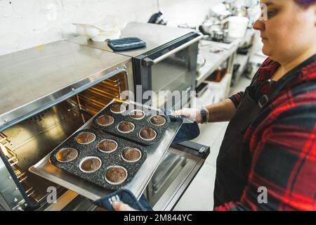 Die Chefköchin nimmt Schokoladen-Muffins aus dem Ofen und bereitet Süßigkeiten zu. Hochwertiges Foto Stockfoto