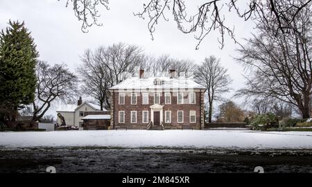 Ein zweistöckiges Ziegelgebäude im Winter mit schneebedeckten Bäumen Stockfoto