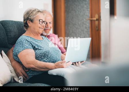 Seniorenpaar zu Hause, das sich mit einem Laptop entspannen kann. Neuer moderner Lebensstil für ältere Rentner. Mann und Frau mit Computer und Internetanschluss Stockfoto