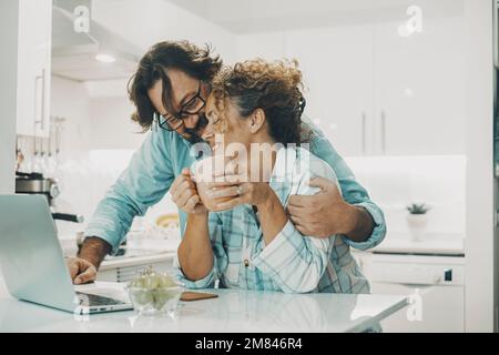 Ein Mann, der eine Frau zu Hause in der Küche mit Liebe umarmt. Freizeitaktivität im Innenbereich und Beziehungsleben. Verheiratete genießen die Zeit. Ein junges Paar usi Stockfoto