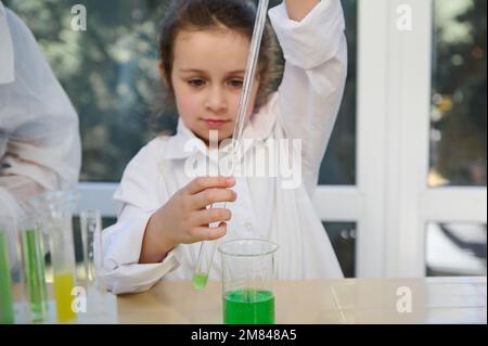 Details: Hände des Schulkindes mit einer graduierten Pipette, Tropfen einiger Reagenzien in ein Reagenzglas mit chemischer Flüssigkeitssubstanz Stockfoto