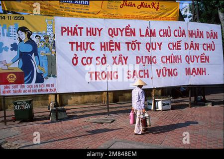 Eine Frau mit konischem Hut, die am Wahlschild vorbeigeht, aufgenommen 1999, Hanoi, Vietnam Stockfoto