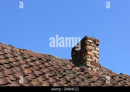 Dachterrasse mit alten Fliesen und einem Steinkamin vor einem blauen Himmel Stockfoto