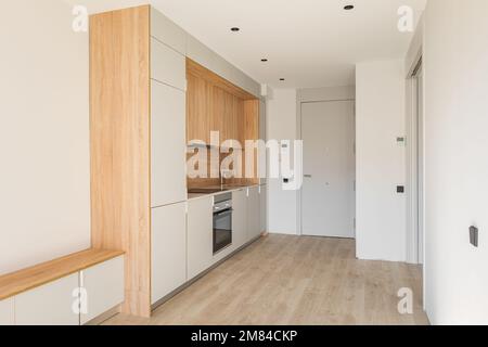 Einfacher, kleiner modularer Küchenbereich an der Wand im Studio-Apartment neben der Eingangstür. Möbelminimalismus mit vielen Schränken, einem Ofen und einem Stockfoto