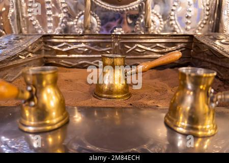 Kaffeemaschine in heißem Sand. Traditionelle orientalische Methode der Kaffeezubereitung. Der Vorgang der Zubereitung eines Getränks. Stockfoto