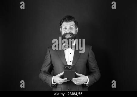 Stauned glücklich Mann in Smoking Fliege mit Geschäft Belohnung Box. Anlass Gruß. Stockfoto