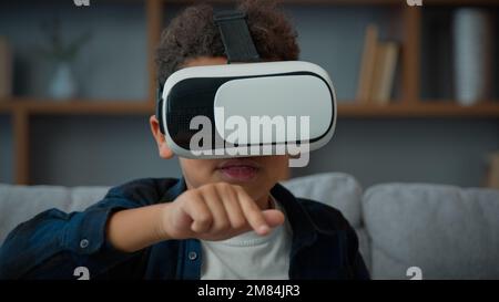 Kleiner afroamerikanischer ethnischer Junge Schüler Sohn Kind Schuljunge zu Hause trägt VR-Brille und spielt Online-Video 3D-Spiele Bildung lernen mit Stockfoto