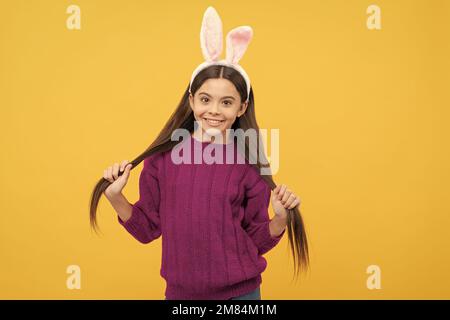 Fröhliches Teenager-Kind mit Häschenohren, das ihr Haar hält, osterkostüm Stockfoto