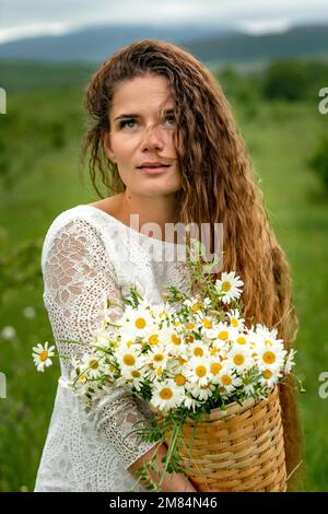 Eine Frau mittleren Alters hält einen großen Strauß Gänseblümchen in den Händen. Wildflowers für Glückwünsche Stockfoto