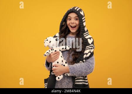 Ein erstaunlicher Teenager. Teenager Mädchen 12, 13, 14 Jahre alt halten weiches Spielzeug zum Geburtstag auf gelbem Hintergrund. Kind mit ihrem Spielzeug. Kinder tragen sie im Herbst oder Winter Stockfoto