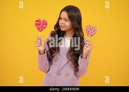 Lustiges Kind mit Lutscher auf gelbem isoliertem Hintergrund. Süßes Kindheitsleben. Teen Mädchen mit yummy Karamell Lollipop, Süßwarenladen. Lustiges Gesicht. Stockfoto