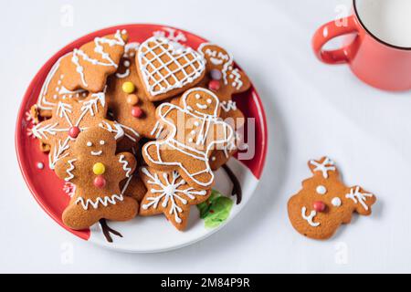 Lebkuchen-Kekse in Form eines Ingwermanns auf rotem Teller. Weißer Hintergrund. Traditionelles Weihnachtsdessert. Verspielt und glücklich. Stockfoto